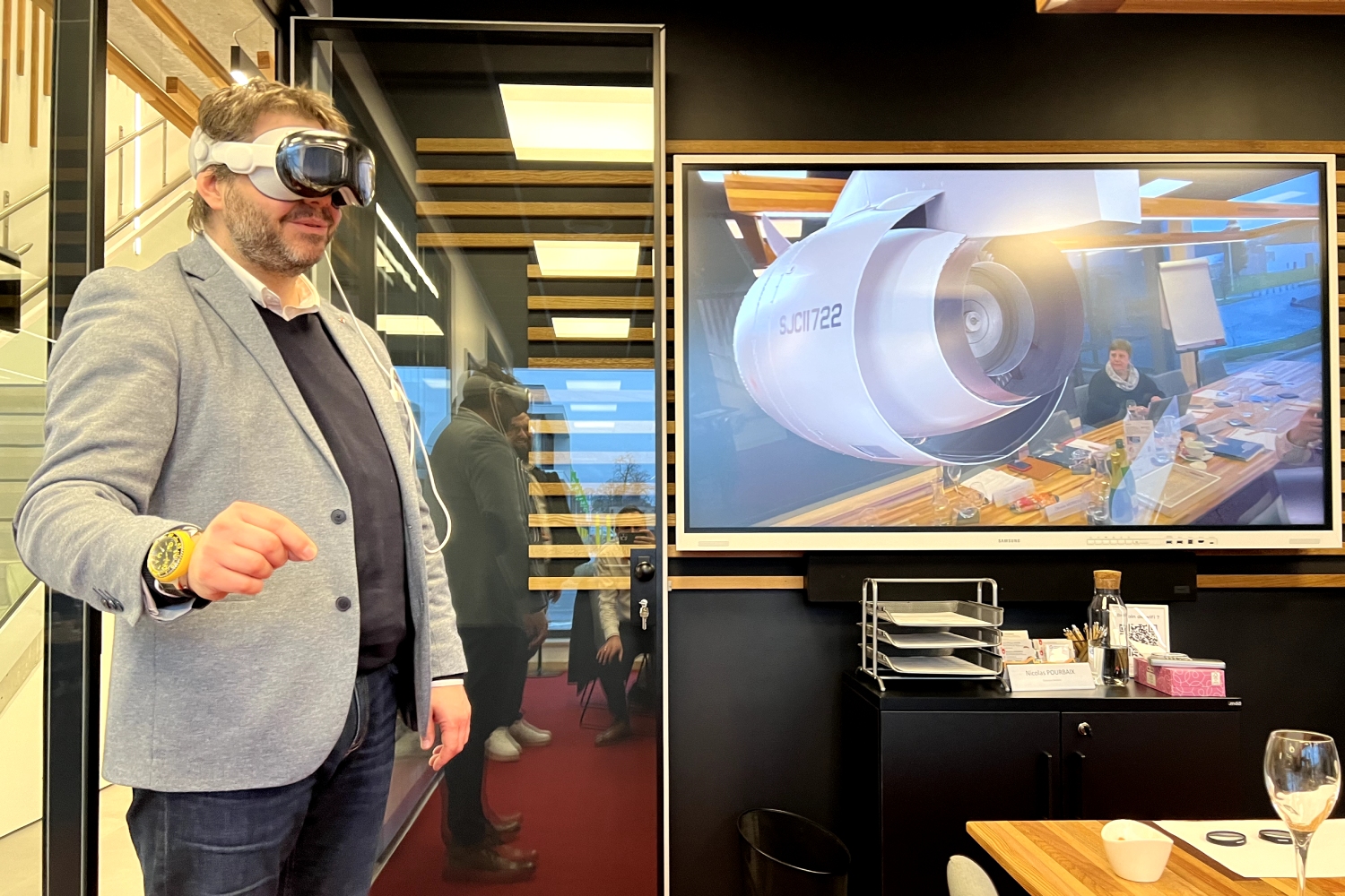 Fabian Martin essayant à son tour le casque VR Apple Vision, expérimentant avec. Le résultat est projeté aux personnes présentes sur l'écran derrière.