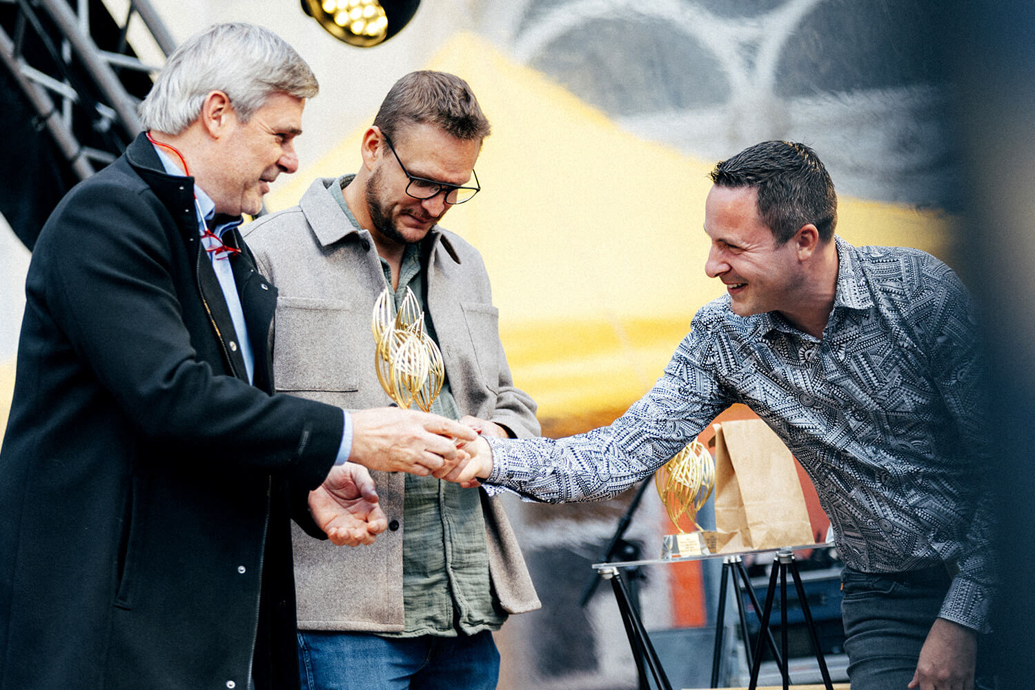 Trois hommes échangent une poignée de main sur scène lors de la remise du Prix du Souffle de l’Innovation. L’un d’eux tient un trophée, symbolisant la reconnaissance de leur engagement.